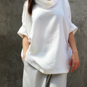 May include: A white linen top with a cowl neck and short sleeves. The top is loose fitting and has a relaxed silhouette.