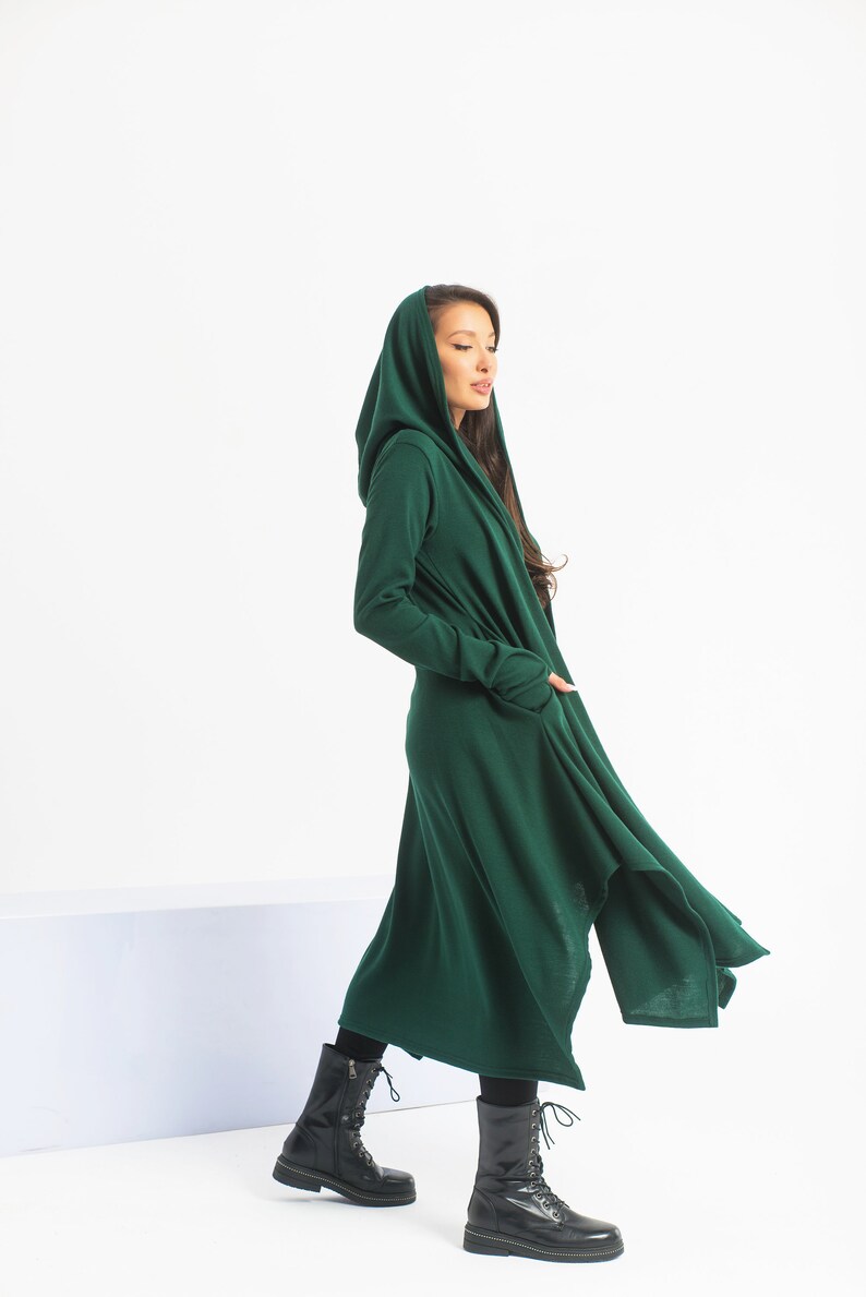May include: A long, dark green hooded cardigan with a flowing, asymmetrical hem. The cardigan is made of a soft, knit fabric and has a relaxed fit.