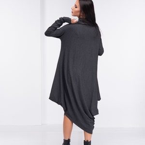 May include: A charcoal gray long-sleeved dress with a cowl neck and a draped asymmetrical hem. The dress is made of a soft, stretchy fabric and is worn with black ankle boots.