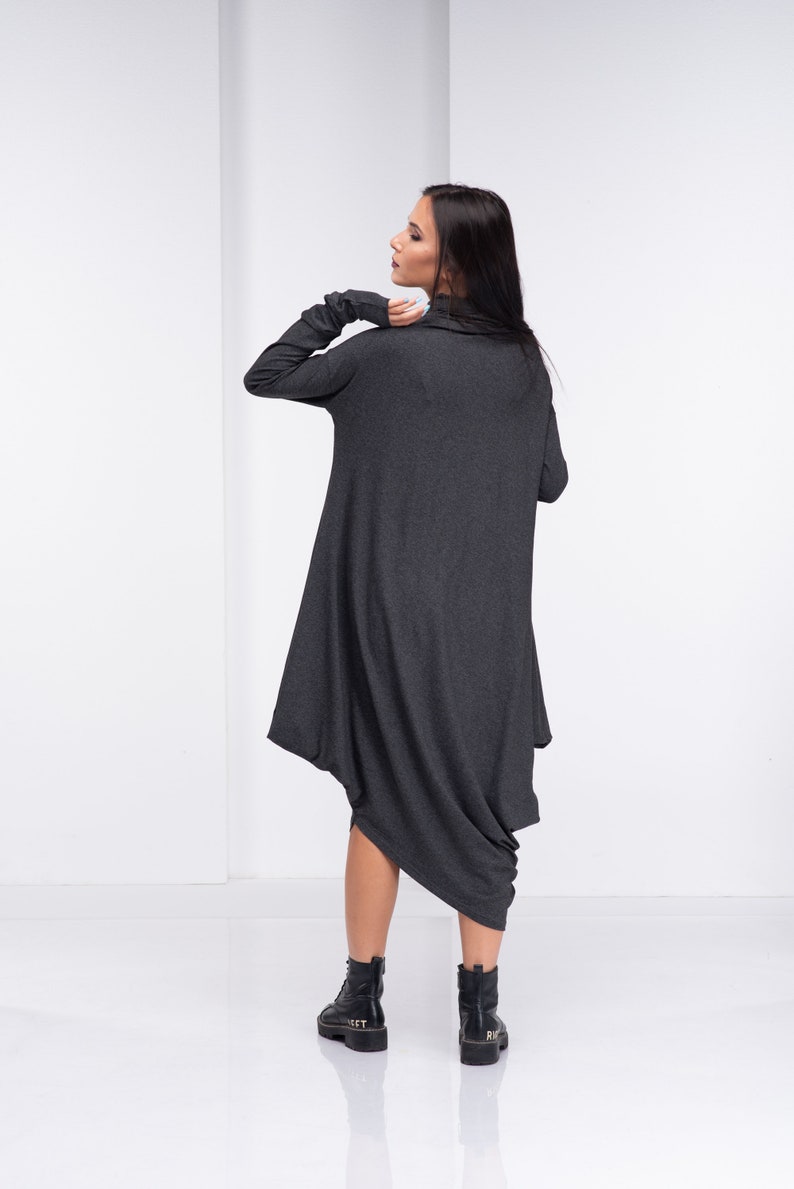 May include: A charcoal gray long-sleeved dress with a cowl neck and a draped asymmetrical hem. The dress is made of a soft, stretchy fabric and is worn with black ankle boots.