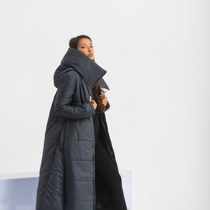 May include: A long, dark blue puffer coat with a large hood and a zipper closure. The coat is quilted and has a fitted silhouette.