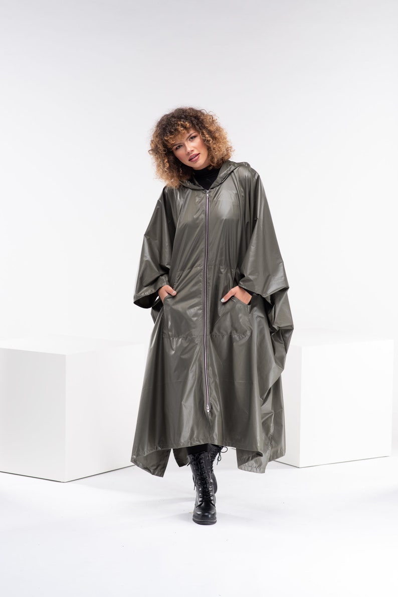 May include: A long, hooded, olive green raincoat with a zipper closure and two pockets. The raincoat is made of a shiny, water-resistant material.