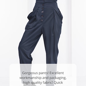 Pu&ograve; includere: Pantaloni blu navy a vita alta con chiusura a bottoni. I pantaloni hanno un'ampia cintura e pieghe sul davanti. La modella indossa una maglietta bianca. I pantaloni sono realizzati in tessuto di alta qualit&agrave;.