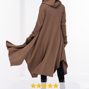 May include: A brown hooded cardigan with long sleeves and a long, flowing hem. The cardigan has thumb holes at the cuffs. The model is wearing the cardigan with black pants and black boots.