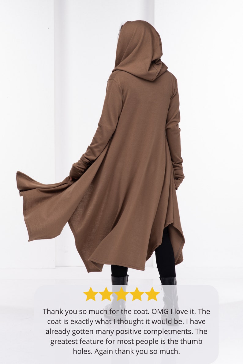 May include: A brown hooded cardigan with long sleeves and a long, flowing hem. The cardigan has thumb holes at the cuffs. The model is wearing the cardigan with black pants and black boots.