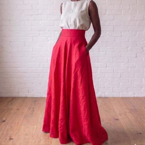 May include: A sleeveless cream-colored top paired with a high-waisted, floor-length red skirt. The skirt features a wide waistband, a full, flowing silhouette, and side pockets. The ensemble is constructed from a textured fabric with visible weave.