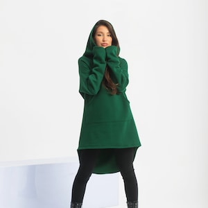 May include: A woman wearing a long, dark green hooded sweatshirt with a high-low hemline and black leggings. She is wearing black lace-up boots.