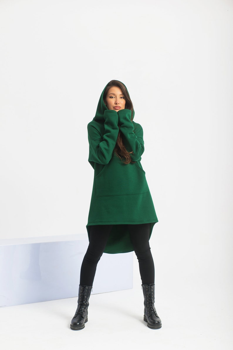 May include: A woman wearing a long, dark green hooded sweatshirt with a high-low hemline and black leggings. She is wearing black lace-up boots.
