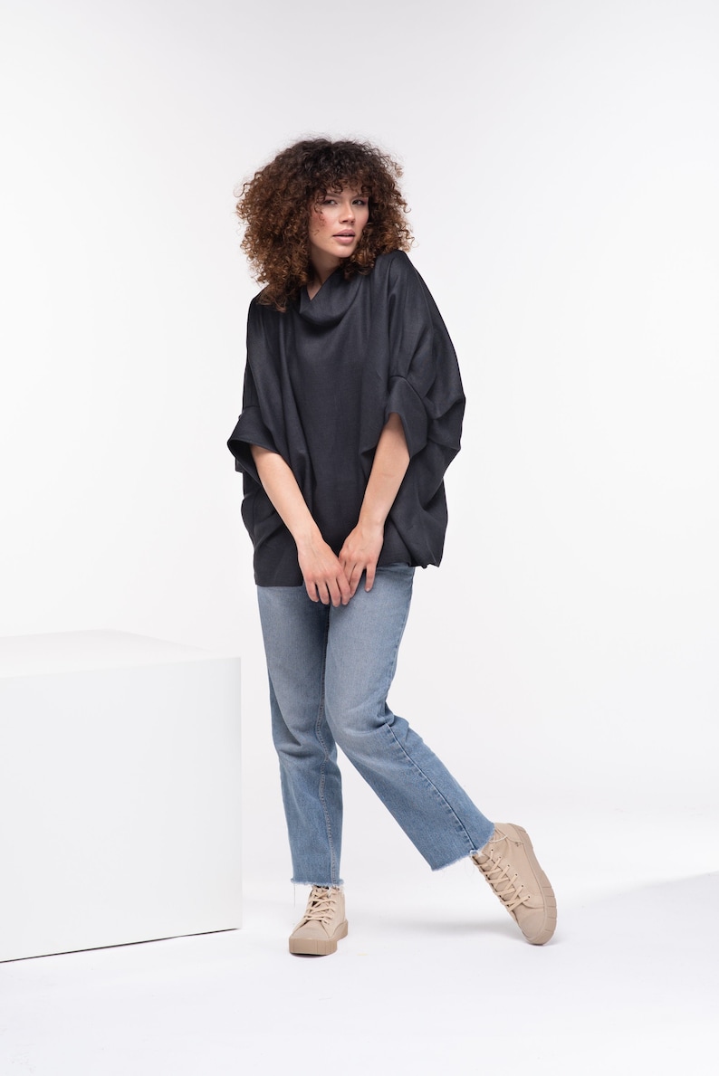 Puede incluir: Una mujer con un top negro holgado de cuello de pico con mangas largas y jeans azules. Lleva zapatillas beige de ca&ntilde;a alta.