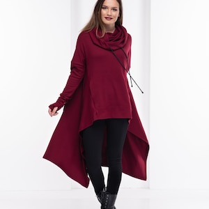 May include: A burgundy high-low tunic sweater with a cowl neck and long sleeves. The sweater has a drawstring at the neck and a high-low hemline.