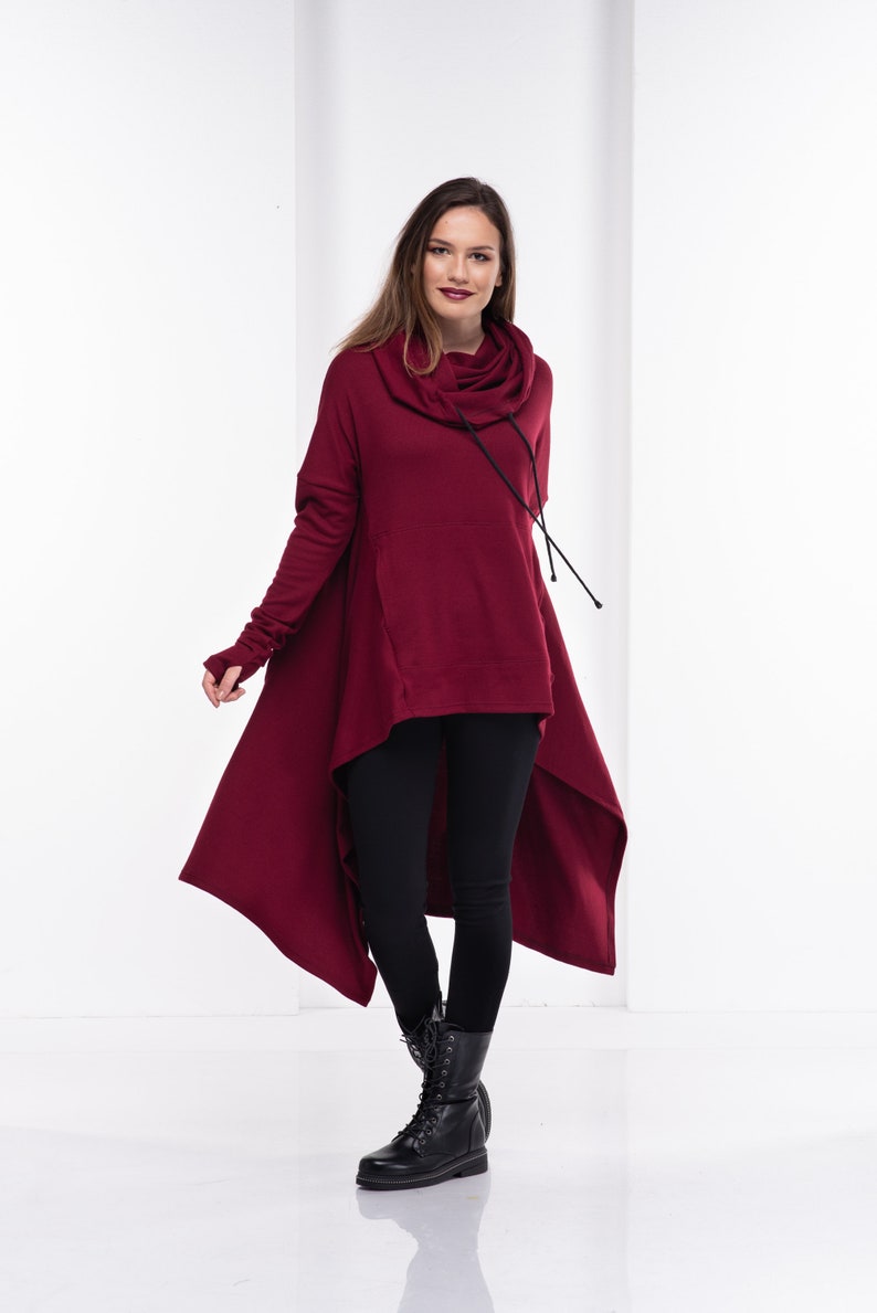 May include: A burgundy high-low tunic sweater with a cowl neck and long sleeves. The sweater has a drawstring at the neck and a high-low hemline.