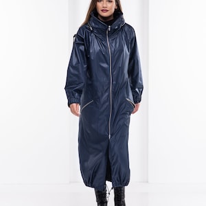 May include: A long, navy blue raincoat with a zipper closure and a high collar. The raincoat has a drawstring at the waist and cuffs. The model is wearing black boots.
