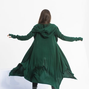 May include: A long, dark green hooded cardigan with long sleeves and a flowing design. The cardigan is made of a soft, knit fabric and has a relaxed fit.