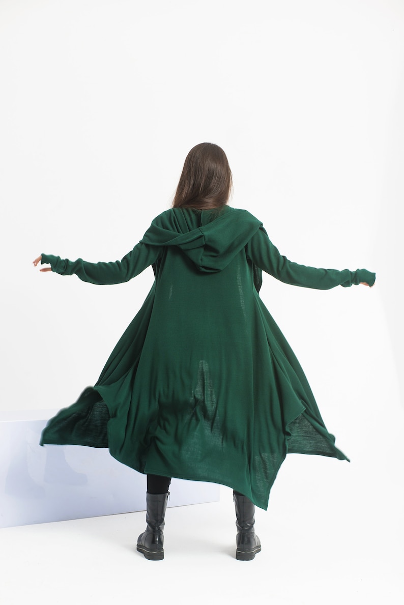 May include: A long, dark green hooded cardigan with long sleeves and a flowing design. The cardigan is made of a soft, knit fabric and has a relaxed fit.
