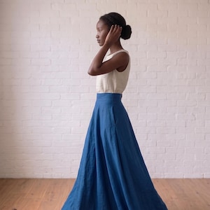 May include: A sleeveless cream-colored top paired with a high-waisted, floor-length blue skirt. The skirt features a wide waistband and a full, flowing silhouette that reaches the floor, while the top is a simple, fitted sleeveless design.