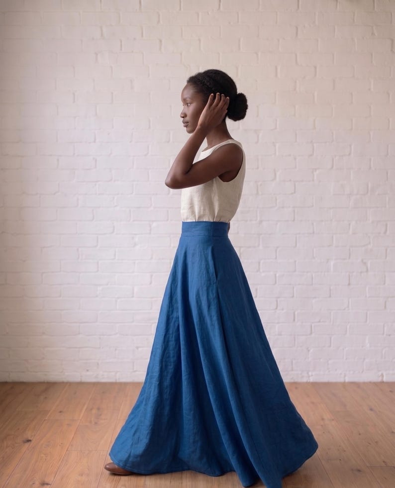 May include: A sleeveless cream-colored top paired with a high-waisted, floor-length blue skirt. The skirt features a wide waistband and a full, flowing silhouette that reaches the floor, while the top is a simple, fitted sleeveless design.