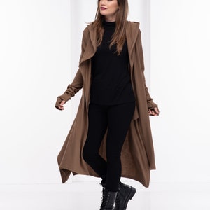 May include: A long brown cardigan with a hood, worn over a black turtleneck and black leggings. The person is wearing black lace-up boots.