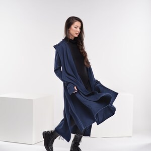May include: A woman wearing a long, navy blue hooded cardigan with a black turtleneck shirt and black boots. The cardigan is open and flowing in the wind.