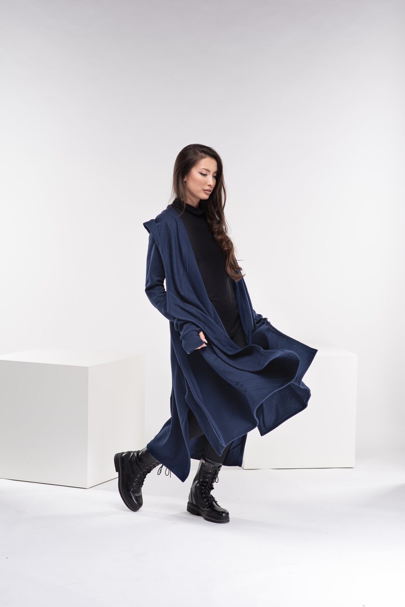 May include: A woman wearing a long, navy blue hooded cardigan with a black turtleneck shirt and black boots. The cardigan is open and flowing in the wind.