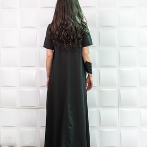 K&ouml;nnte beinhalten: Eine Frau tr&auml;gt ein langes, schwarzes Maxikleid mit kurzen &Auml;rmeln. Das Kleid hat ein schlichtes, flie&szlig;endes Design und ist aus einem weichen, bequemen Stoff gefertigt.
