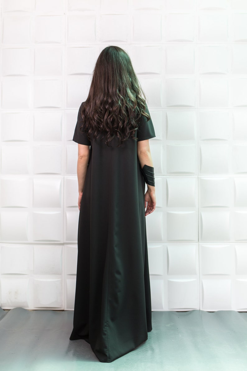 K&ouml;nnte beinhalten: Eine Frau tr&auml;gt ein langes, schwarzes Maxikleid mit kurzen &Auml;rmeln. Das Kleid hat ein schlichtes, flie&szlig;endes Design und ist aus einem weichen, bequemen Stoff gefertigt.