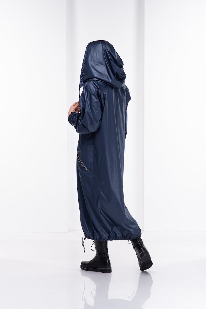 May include: A long, navy blue raincoat with a hood. The raincoat has a zipper down the front and a drawstring at the waist. The model is wearing black boots.