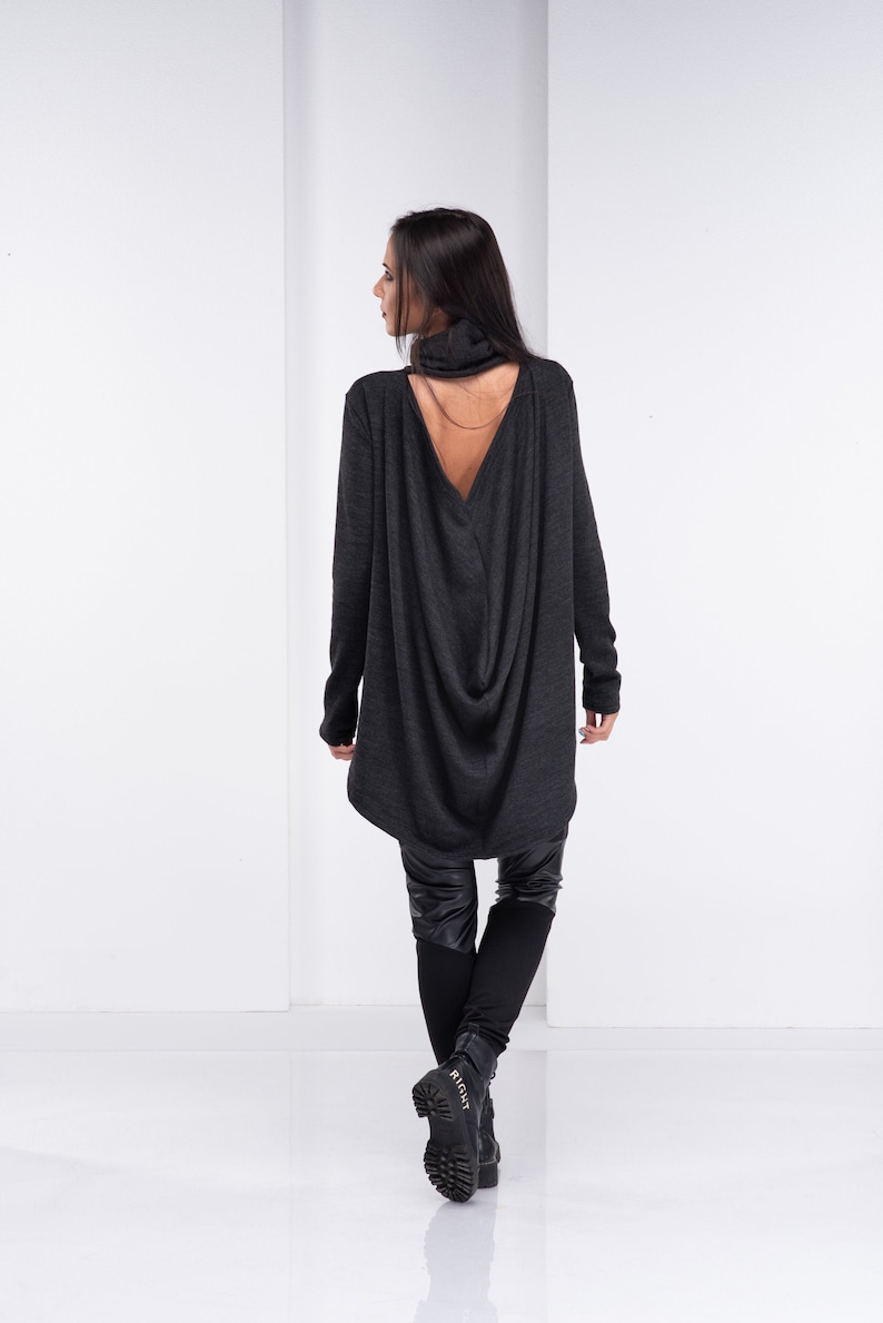 May include: A dark gray long-sleeved shirt with a low back and a draped design. The shirt is worn with black leggings and black boots.