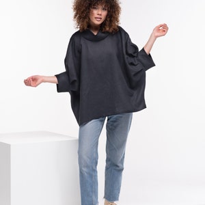 Puede incluir: Una mujer con una camisa negra de cuello alto y un corte holgado y jeans azules. Lleva zapatillas beige de ca&ntilde;a alta.