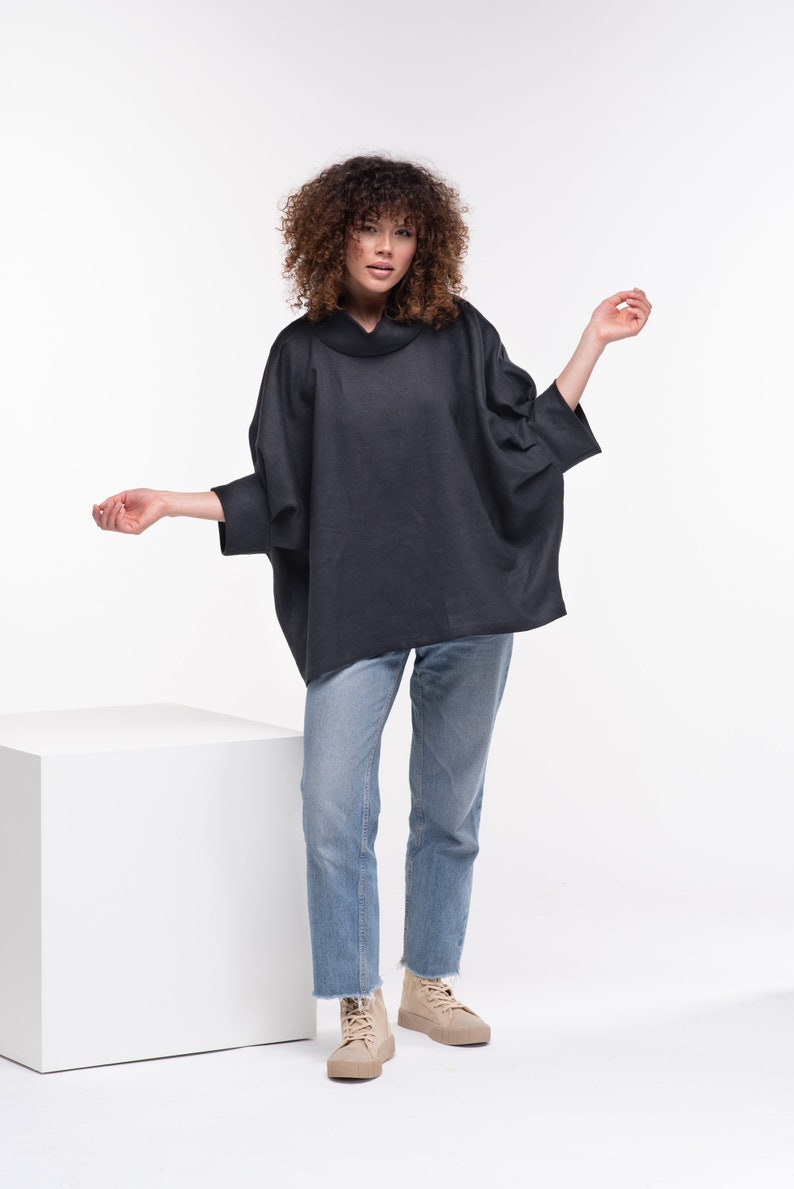 Puede incluir: Una mujer con una camisa negra de cuello alto y un corte holgado y jeans azules. Lleva zapatillas beige de ca&ntilde;a alta.