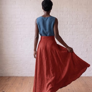 May include: A sleeveless blue linen top paired with a high-waisted, floor-length rust-colored linen skirt. The skirt features a wide waistband and a full, flowing silhouette that flares out at the hem, showcasing the natural texture of the fabric.