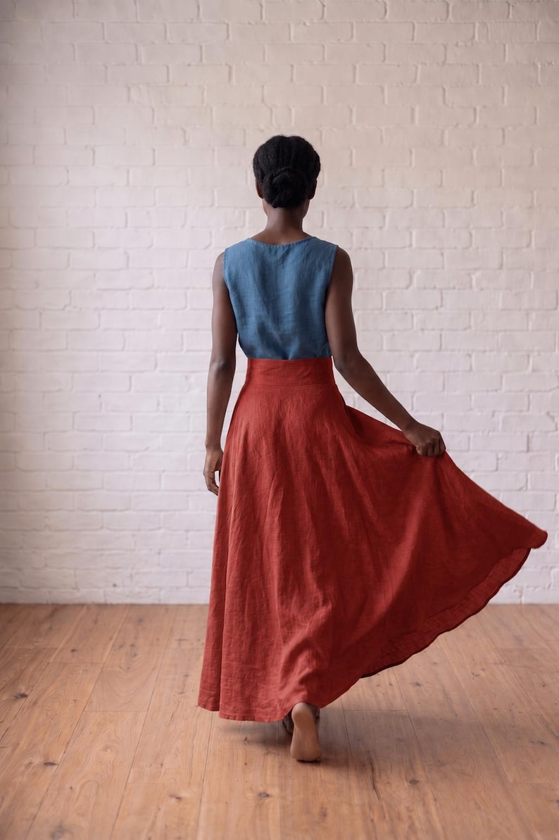 May include: A sleeveless blue linen top paired with a high-waisted, floor-length rust-colored linen skirt. The skirt features a wide waistband and a full, flowing silhouette that flares out at the hem, showcasing the natural texture of the fabric.