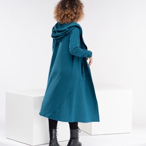 Pu&ograve; includere: Un cardigan color teal con cappuccio, maniche lunghe e un design lungo e fluido. Il cardigan &egrave; realizzato in un tessuto morbido e confortevole e ha una vestibilit&agrave; rilassata.