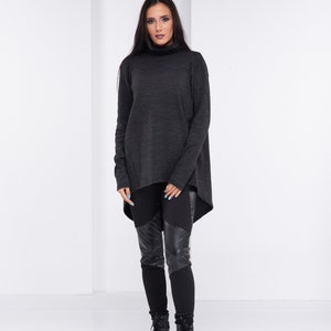 May include: A woman is wearing a dark gray turtleneck sweater with a high-low hemline and black leggings with leather panels. She is wearing black combat boots.