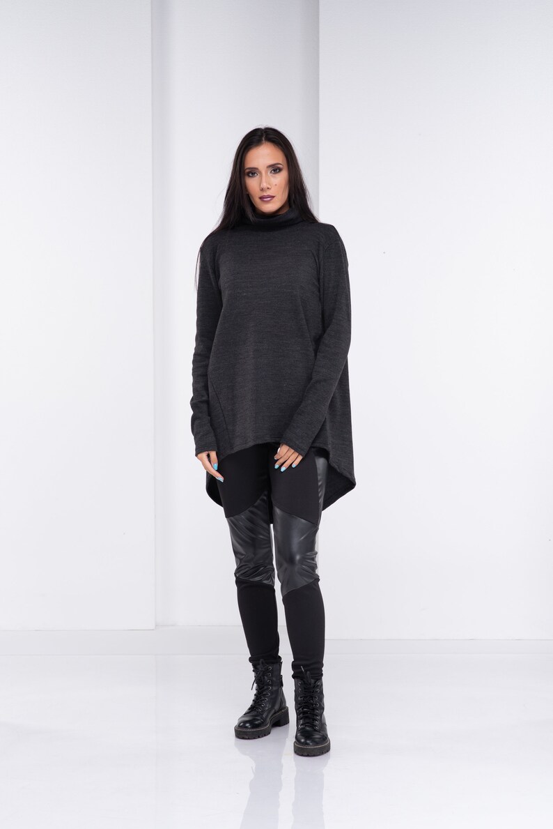 May include: A woman is wearing a dark gray turtleneck sweater with a high-low hemline and black leggings with leather panels. She is wearing black combat boots.