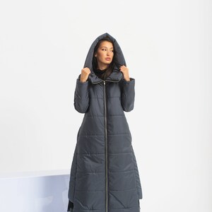 May include: A long, dark blue quilted coat with a hood. The coat has a zipper closure and a high collar.