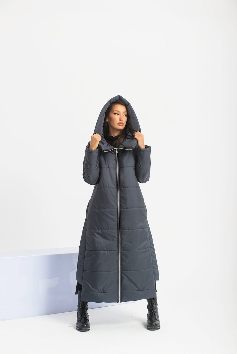 May include: A long, dark blue quilted coat with a hood. The coat has a zipper closure and a high collar.
