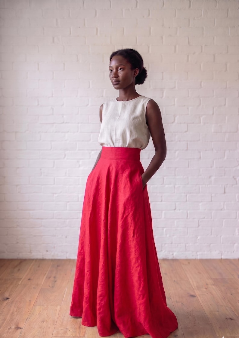 May include: A sleeveless beige top with a round neckline paired with a high-waisted, floor-length red skirt. The skirt features a wide waistband and side pockets, creating a full, flowing silhouette that reaches the floor in a solid red color.