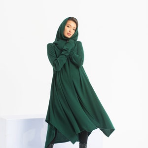 May include: A long, dark green hooded dress with a flowing skirt. The dress is made of a soft, comfortable fabric and has a relaxed fit. The model is wearing black boots.