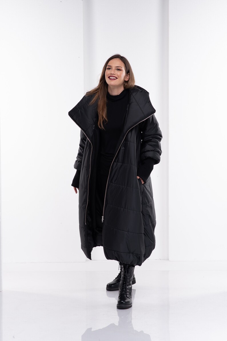 May include: A black puffer coat with a large collar and a zip closure. The coat is long and has a relaxed fit. The model is wearing black boots.