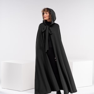 May include: A long, dark green hooded cape with a tie at the neck. The cape is made of a soft, flowing fabric.