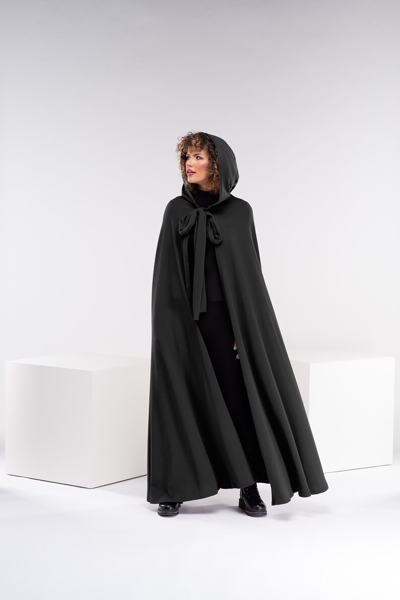 May include: A long, dark green hooded cape with a tie at the neck. The cape is made of a soft, flowing fabric.
