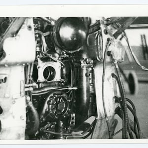 May include: Black and white photo of a vintage aircraft engine with exposed parts and wires. The engine is partially disassembled, revealing the inner workings of the engine.