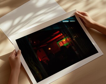 Könnte beinhalten: Ein rechteckiger Fotodruck, der eine schwach beleuchtete Innenszene mit einem leuchtend grünen Neonschild mit chinesischen Schriftzeichen zeigt. Das Bild ist von einem weißen Rand umgeben und präsentiert eine dunkle Atmosphäre mit roten Akzenten.