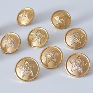 May include: A selection of gold-coloured metal buttons. Each button features a star with a hammer and sickle emblem. The buttons are round and have a slightly raised design.