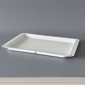 May include: A rectangular white enamel tray with slightly raised edges. The tray has a smooth surface and shows signs of wear with small areas of black paint loss. The tray is designed for serving or display.
