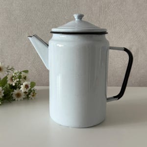 May include: A light blue enamelware coffee pot with a lid and a black handle. The spout and rim are also black. The pot is sitting on a white surface. The pot is approximately 9 inches tall.