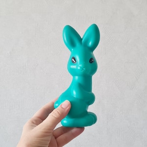 May include: A teal blue plastic rabbit toy with black eyes. The rabbit is standing upright with its ears perked up.