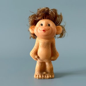 Puede incluir: Una muñeca de mono vintage con una cara sonriente, cabello castaño y un cuerpo bronceado. La muñeca tiene orejas grandes y una boca pequeña roja. El mono está de pie con los brazos a los lados. La muñeca está hecha de un material suave.