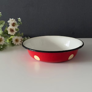 Puede incluir: Un cuenco de esmalte rojo con interior blanco y ribete negro. El cuenco presenta lunares amarillos en el exterior. Un artículo de menaje para servir.