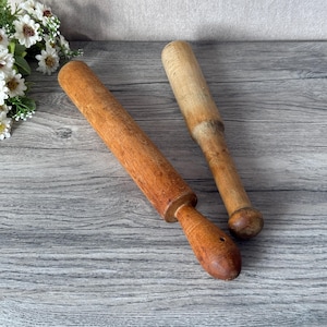 Puede incluir: Dos rodillos de amasar de madera, uno más largo y delgado que el otro, sobre una superficie de madera gris.